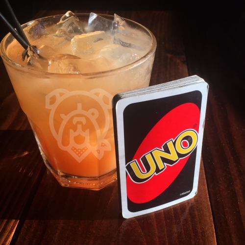 A glass of iced drink next to a UNO card on a wooden table.