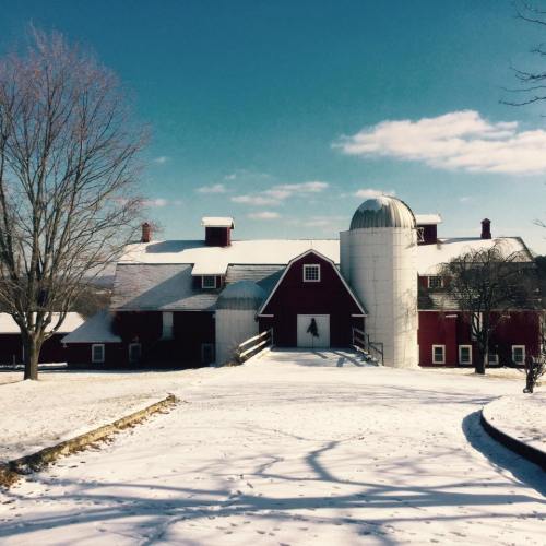 A red barn and silos surrounded by snow under a clear blue sky, with a path leading to the entrance.