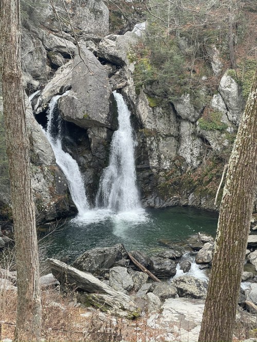 A serene waterfall cascades into a rocky pool, surrounded by trees and rugged cliffs.