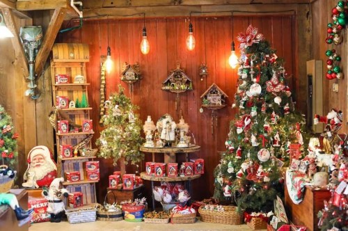 A cozy holiday display featuring decorated trees, ornaments, and festive decorations in a rustic wooden setting.