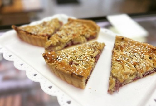 Four slices of almond-topped tart on a white plate, dusted with powdered sugar.