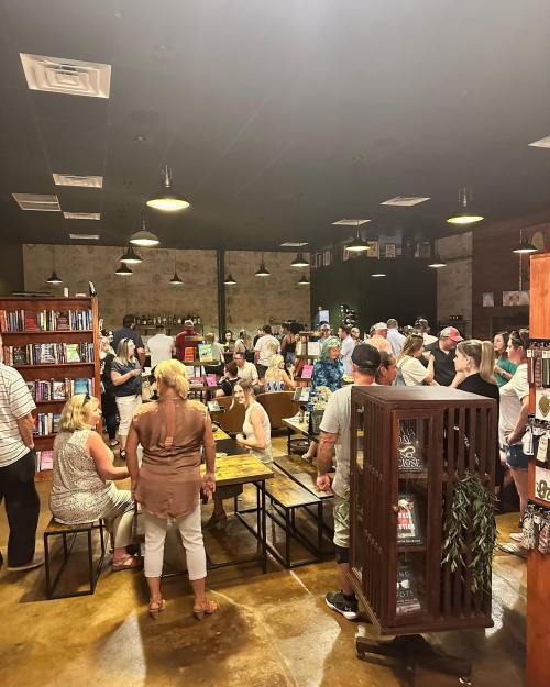 A crowded bookstore with people browsing and socializing among shelves of books and a cozy atmosphere.