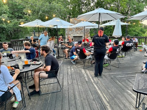 A lively outdoor dining area with people seated at tables under umbrellas, enjoying food and drinks.