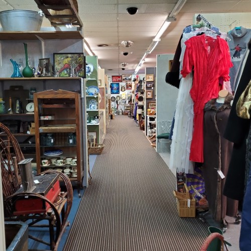 A narrow aisle in an antique store lined with various vintage items, including furniture, clothing, and decor.