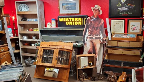 A vintage shop filled with antiques, including a cowboy cutout, wooden furniture, and a Western Union sign.