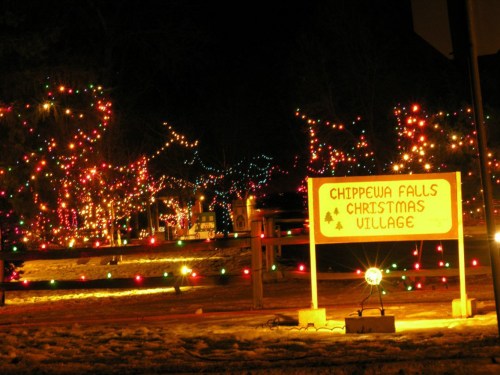 A festive display of colorful Christmas lights at Chippewa Falls Christmas Village, with a sign illuminated at night.