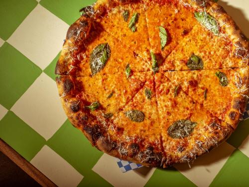 A freshly baked pizza with melted cheese, basil leaves, and a golden crust, sliced into eight pieces on a checkered table.