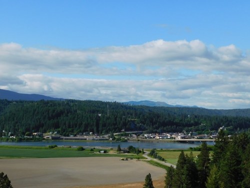 A scenic view of a river surrounded by green hills and fields under a blue sky with scattered clouds.