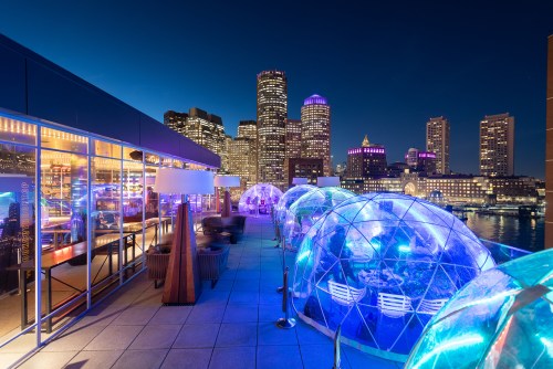 Rooftop view with illuminated igloo-like structures and a city skyline at night.