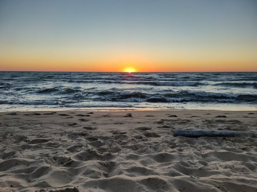 Sunset over the ocean, with gentle waves lapping at a sandy beach under a colorful sky.
