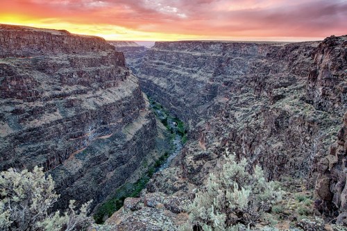 A stunning canyon landscape at sunset, with layered rock formations and a winding river below.