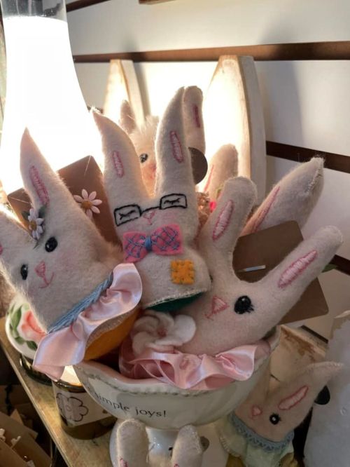 A collection of cute, handmade felt bunnies in a decorative bowl, featuring various colors and accessories.