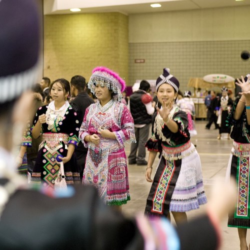 A group of women in colorful traditional attire participate in a cultural dance at an indoor event.