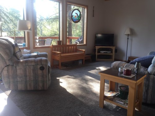 Cozy living room with two armchairs, a wooden bench, a TV, and large windows letting in natural light.
