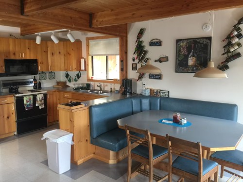 A cozy kitchen with wooden cabinets, a dining table, and wine bottles displayed on the wall.
