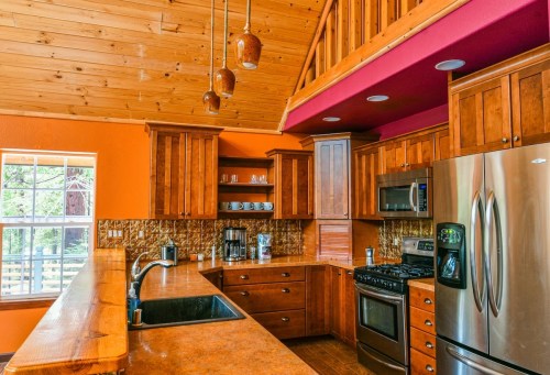 Bright kitchen with wooden cabinets, stainless steel appliances, and a high ceiling, featuring orange walls and a cozy atmosphere.