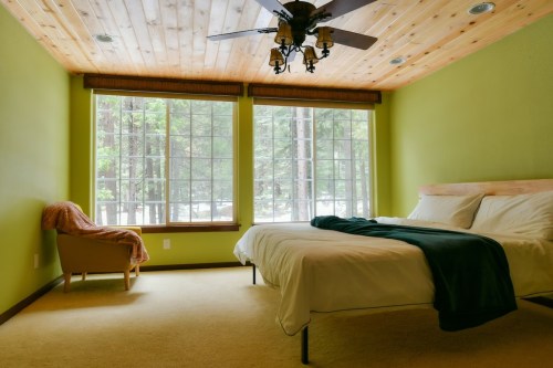 Cozy bedroom with green walls, a large window, a bed with white linens, and a chair in a serene, wooded setting.