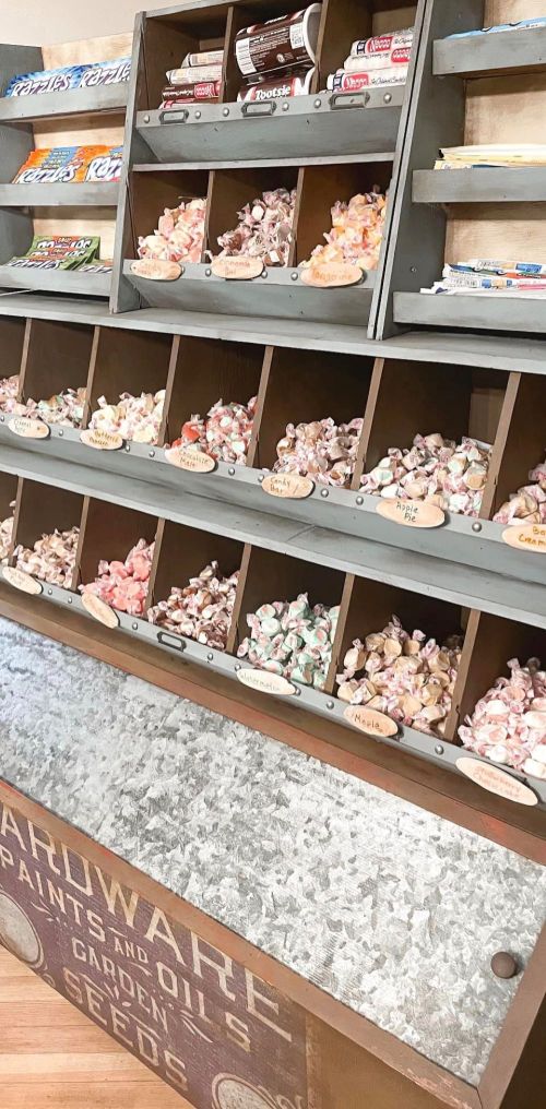 A vintage display with wooden bins filled with colorful candies and labeled jars, set against a rustic backdrop.
