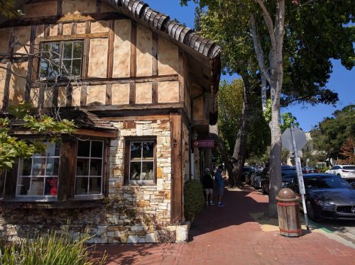 A charming, rustic building with stone and wood accents, surrounded by trees and parked cars on a sunny day.