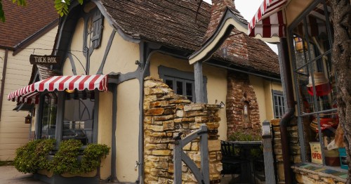 Charming cottage with a thatched roof, stone accents, and striped awnings, featuring a cozy outdoor seating area.
