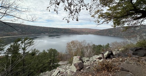 A serene lake surrounded by autumn foliage and rocky terrain, under a cloudy sky.