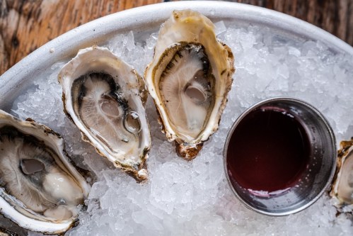 Fresh oysters on ice served with a small bowl of sauce.