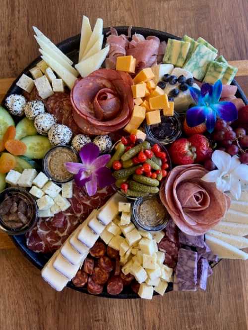 A colorful charcuterie board featuring various cheeses, meats, fruits, and garnishes arranged artfully.