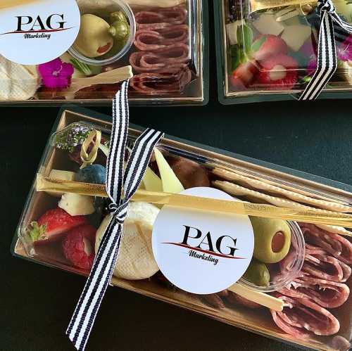 A gourmet charcuterie box with meats, cheeses, fruits, and olives, tied with a black and white ribbon.