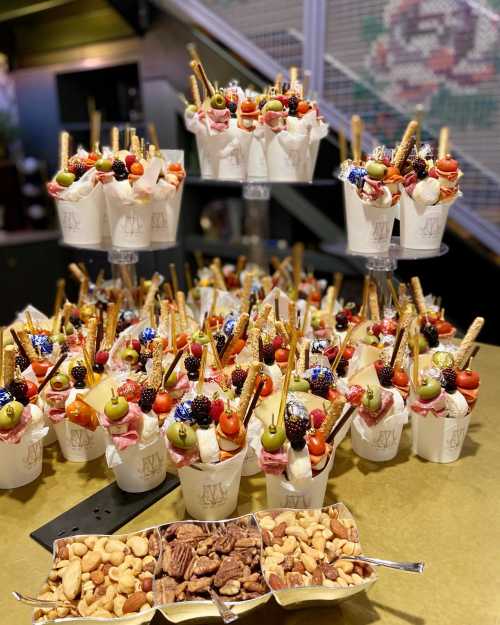 A display of colorful dessert cups topped with fruits, candies, and wafer sticks, alongside a tray of mixed nuts.