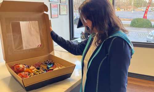 A woman looks at a large box filled with assorted snacks and treats, smiling in a bright indoor setting.