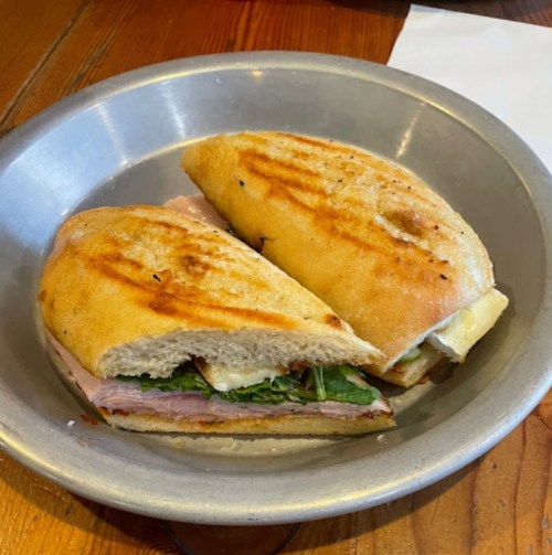 A toasted sandwich cut in half, filled with ham, greens, and cheese, served on a metal plate.