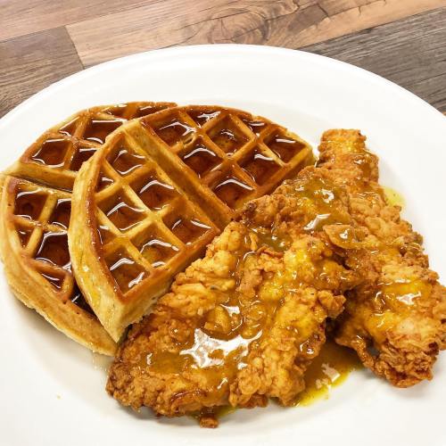 A plate of crispy fried chicken served with two waffles drizzled in syrup.