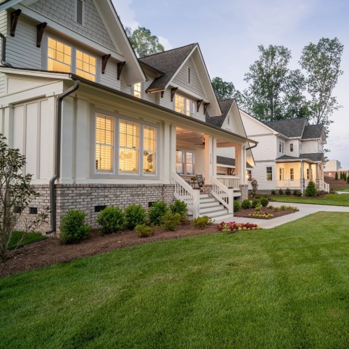 A charming suburban home with a porch, large windows, and a well-maintained lawn, surrounded by trees.