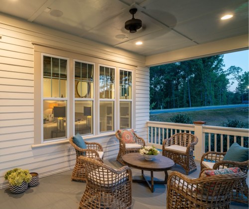 Cozy porch with wicker chairs, a round table, and soft lighting, surrounded by trees at dusk.