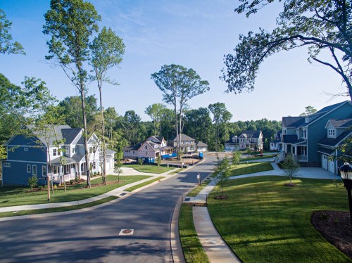 A peaceful suburban neighborhood with new homes, trees, and a clear blue sky.