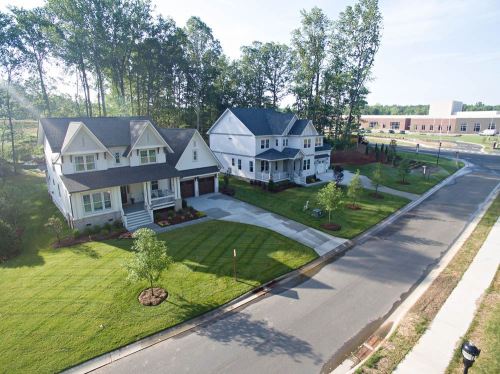 Aerial view of three modern homes on a quiet street, surrounded by green lawns and trees.