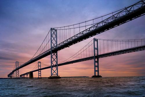 A large suspension bridge spans over water, with a colorful sunset sky in the background.