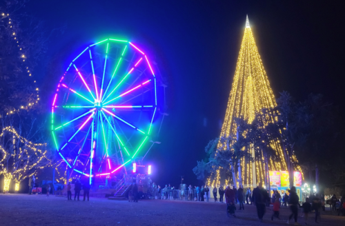 A vibrant night scene featuring a colorful Ferris wheel and a tall, illuminated Christmas tree, with people enjoying the festivities.