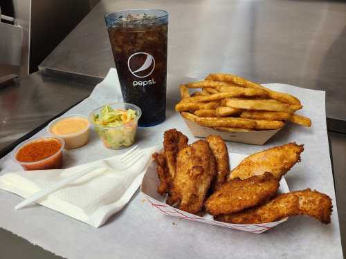 A meal featuring fried fish, fries, coleslaw, dipping sauces, and a Pepsi in a cup on a tray.