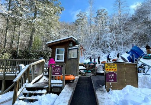 A snowy scene at a water slide entrance with lanes marked, people preparing to slide down in winter attire.
