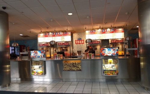 A movie theater concession stand with popcorn, snacks, and drinks, featuring a retro design and bright signage.