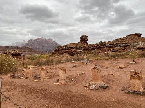 A desolate graveyard with weathered tombstones, surrounded by rocky terrain and cloudy skies in the background.