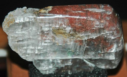 A clear crystal with reddish-brown mineral inclusions, showcasing a unique texture and natural formation.
