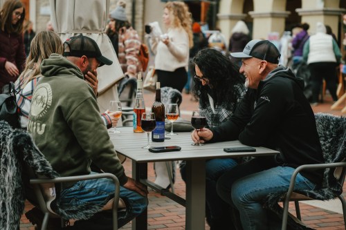 A group of four people enjoying drinks at an outdoor table, laughing and chatting in a lively setting.