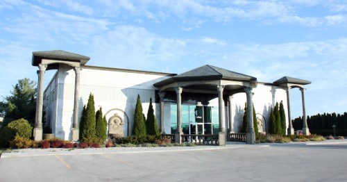 A modern building with a stone facade, tall columns, and landscaped greenery in front under a clear blue sky.