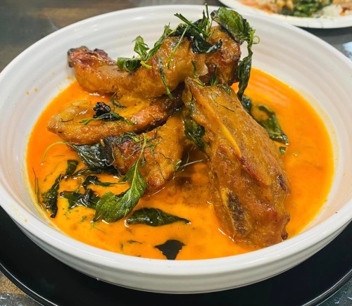 A bowl of chicken wings in a rich, orange curry sauce, garnished with fresh herbs and green leaves.