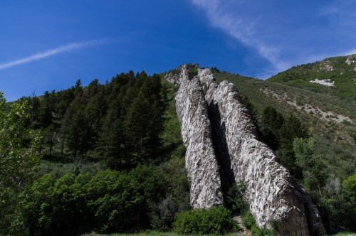A rocky cliffside with tall, jagged formations, surrounded by green trees and a clear blue sky.