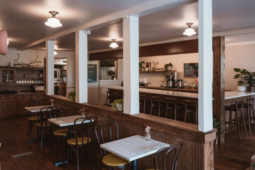 Cozy café interior with wooden accents, small tables, and a counter, featuring plants and warm lighting.
