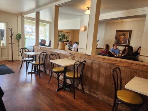 A cozy restaurant interior with wooden accents, tables, and chairs, featuring diners enjoying their meals.