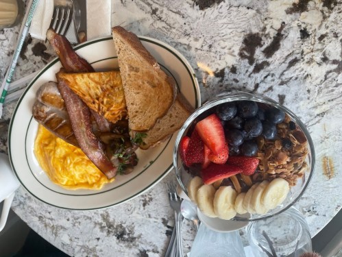 A breakfast plate with eggs, bacon, toast, and a fruit parfait with granola, strawberries, blueberries, and banana slices.
